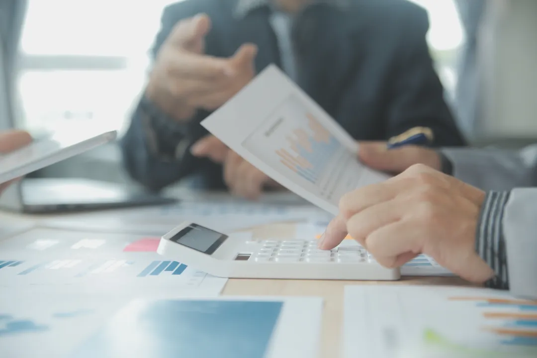 A group of professionals reviewing documents and calculating data using a calculator during a business meeting.